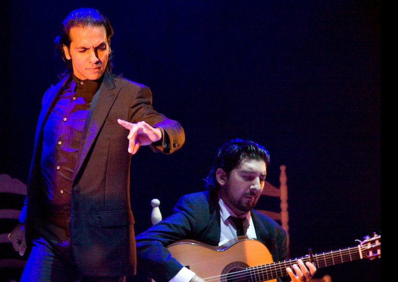 Farruquito onstage with a guitarist performs in an all black suit